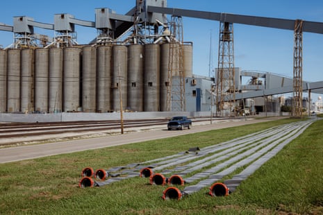 View of pipeline parts in grass, large tanks in the background